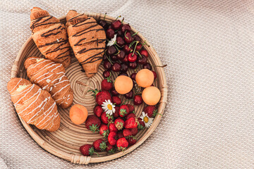 tray with croissants, strawberries, cherries and apricots on a blanket