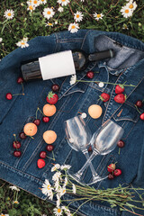 a bottle of wine, two glasses, cherries, strawberries on a denim jacket in a chamomile field