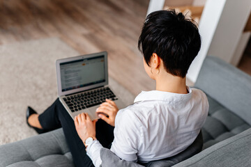 Top view of beautiful young woman holding the laptop working on couch at home