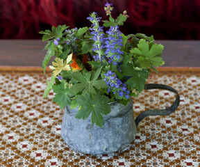 Colorful wild flowers arranged in a copper vessel on a patterned tablecloth in a country house.