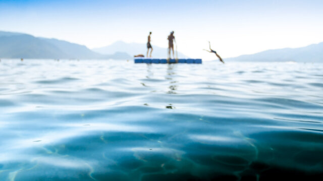 Blurred photo of children jumping from the pontoon into the sea water