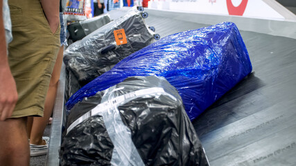Closeup image of wrapped suitcases lying on the luggage claim line at airport