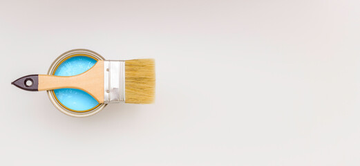 Paint brush with a wooden handle on a can of blue paint, top view. White background, free space for text.