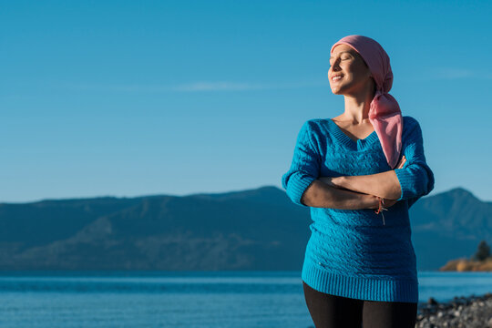 Woman with cancer wears a pink headscarf and with her arms crossed and smile