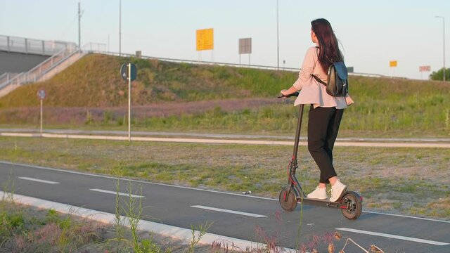 Young beautiful woman rides an electric scooter through an urban settlement.