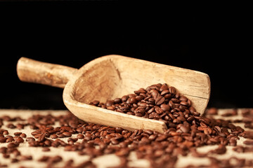 Roasted coffee beans closeup in a wooden scoop on a dark background, selective focus, service