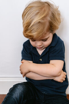 Annoyed blond little boy in casual clothes sitting on the floor with crossed arms