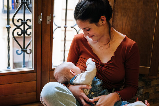 Happy mother breastfeeding baby near window