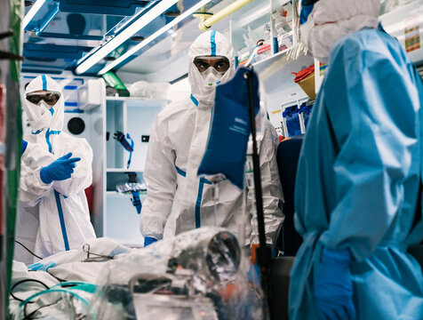 Group of professional doctors in protective uniform standing in ambulance car with equipment and preparing for patient transportation