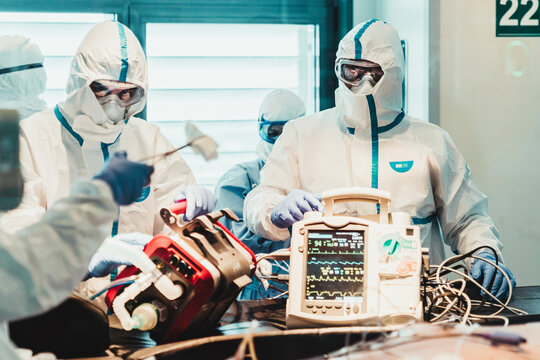 Group of professional doctors wearing protective masks and suits standing near operating table with equipment and preparing for operation in modern clinic