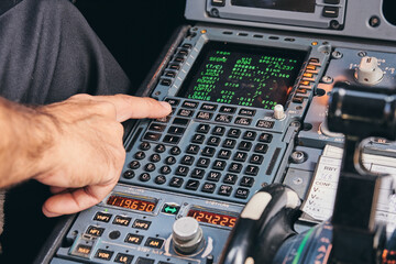 Crop anonymous male pilot using keyboard of flight management system in cockpit of modern aircraft during flight