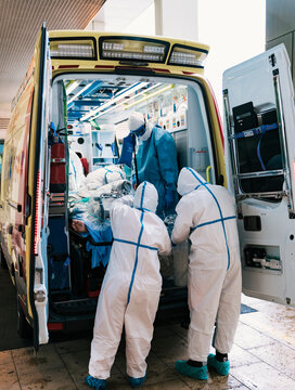 Group of professional doctors in protective uniform standing in ambulance car with equipment and preparing for patient transportation