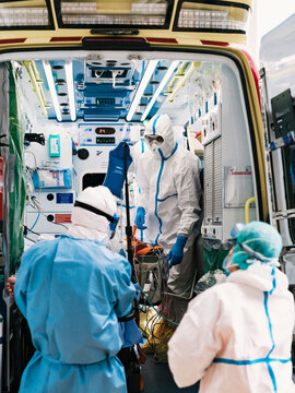 Group of professional doctors in protective uniform standing in ambulance car with equipment and preparing for patient transportation