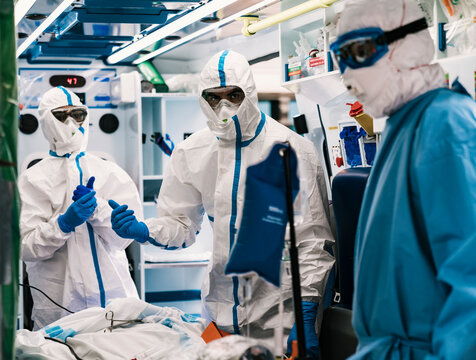 Group of professional doctors in protective uniform standing in ambulance car with equipment and preparing for patient transportation