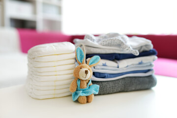 A pile of baby clothes, disposable diapers and a toy rabbit. Parenting expenses concept. Working out a baby budget. Saving money when planning for a newborn.