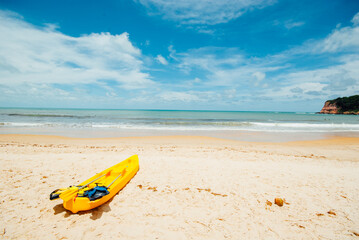 Yellow kayak on a sandy beach in Brazil ready for paddlers in sunny day, active tourism and water recreation.