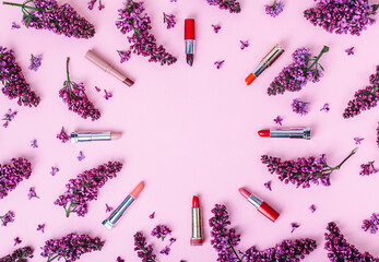 Beauty background lipsticks and lilac flowers on a pastel pink background.