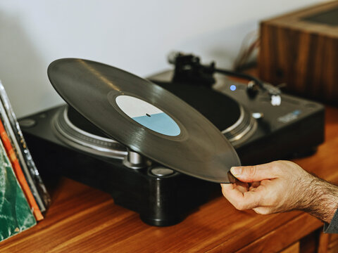 Cropped unrecognizable person setting turntable and enjoying songs on retro vinyl disc while chilling at home