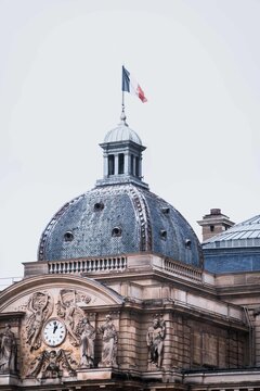 Famous historical buildings roof of breathtaking architecture monument Luxembourg Palace with magnificent statue city clock on wall and waving French flag at top of tower in Luxembourg garden on daytime