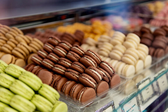 Many colorful tasty macaroons of different colors with various fillings and tastes assorting by colors into containers standing on show window in pastry shop