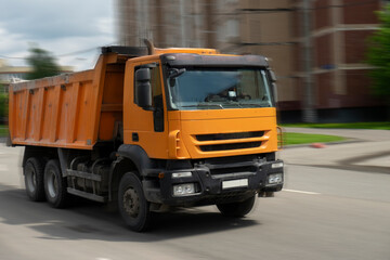 Fototapeta na wymiar Orange dump truck rides on the road to work