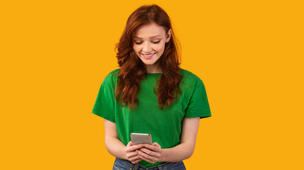 Girl Using Smartphone Playing Mobile Game On Yellow Studio Background