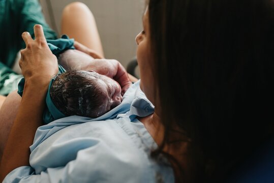 High angle of cheerful adult woman embracing newborn child covered with blood after giving birth in delivery room of contemporary hospital