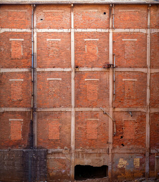 Fototapeta Shabby old high wall of abandoned red brick building with brick windows ruined entrance and pipes with dirty black smudges
