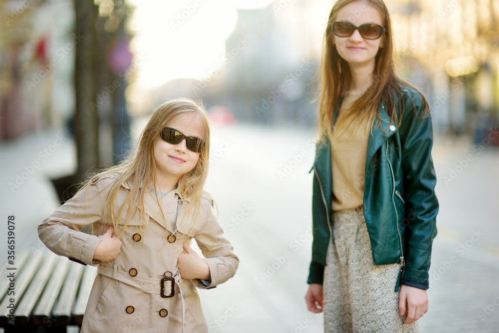 Wall mural two cute young sisters having fun together on beautiful spring day in a city. active family leisure 