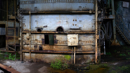 Shabby old ownerless high metal structure with rust layer painted in blue with small steel ajar door and protruding wires on abandoned coal mine