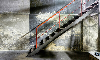 Side view of metal gray dusty staircase with red railing on background of old concrete shabby wall in abandoned factory