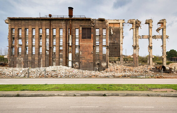 Ruins of old abandoned industrial construction with pipe and piles of trash located near road against cloudy sky in Spain
