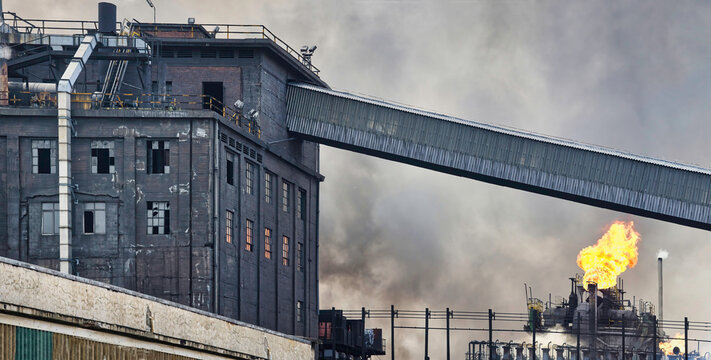 Weathered industrial buildings and pipes emitting smoke and flames at coking factory