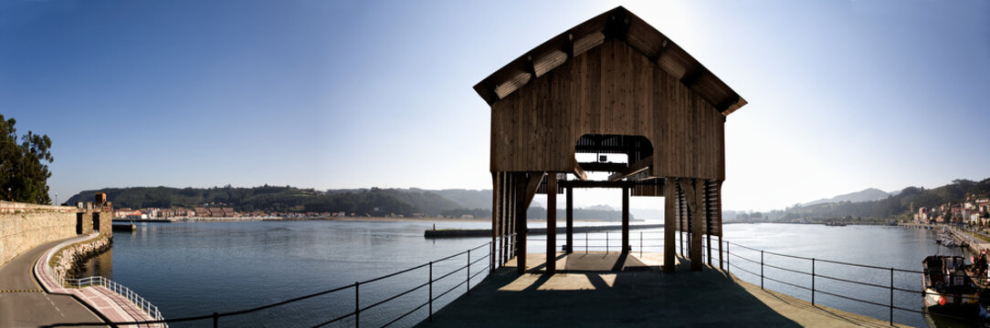 Wide angle view of wooden gazebo located on pier near tranquil sea water in Port of San Esteban de Pravia on sunny day in Spain