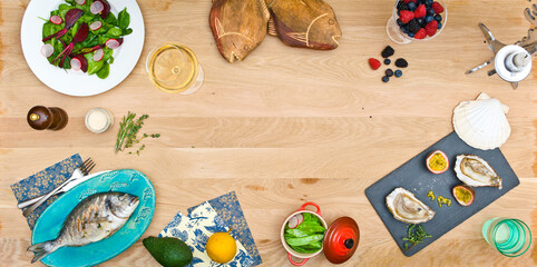 Top view of a light wooden table with sea bass and oysters. And a warm spinach salad. Empty middle of the frame