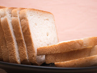 Sliced stack of bread on plate. Background of wooden table. Bread for sandwich. Close up of golden slices in plate.