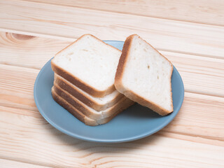 Sliced stack of bread on blue plate. Background of wooden table. Bread for sandwich. Golden slices in plate.