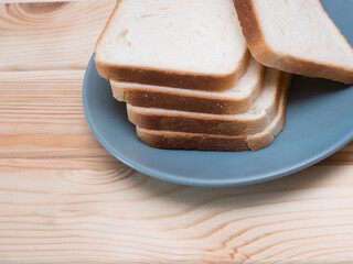 Sliced stack of bread on blue plate. Background of wooden table. Bread for sandwich. Golden slices in plate.