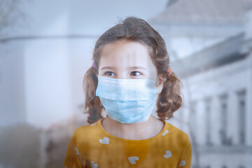 Through glass view of little girl with pigtails in protective mask wearing colorful yellow clothes standing in medical room and looking away