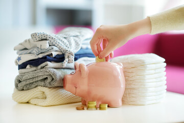 A pile of baby clothes, disposable diapers and a piggy bank. Parenting expenses concept. Working...