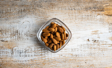 Almonds in a small plate on a vintage wooden table. Almond is a healthy vegetarian protein nutritious food. Natural nuts snacks.