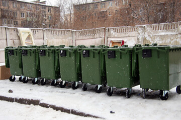 row of green garbage cans in a garbage bin in winter during snowfall