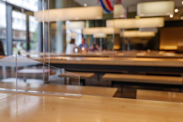 Selected focus view at temporary transparent acrylic partition on wooden table to make Social Distancing in reopening Restaurant during epidemic of COVID-19 with New Normal concept.  