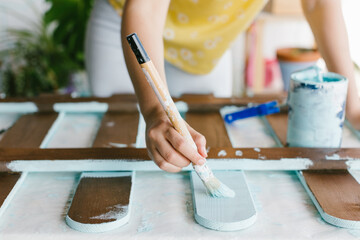 Close-up view of a hand of a person painting a fence with turquoise paint.