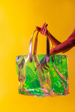 Anonymous female with colorful transparent plastic bag on yellow background in studio