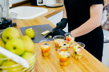 Crop woman in black apron and gloves chopping fresh green apples with knife and preparing healthy fresh desserts in modern kitchen