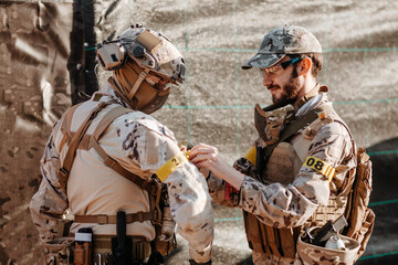 Bearded man in camouflage fastening identification band of arm of squadmate while preparing to play airsoft game together