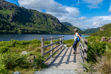 Fototapeta na wymiar A solo female hiker resting on a bridge while looking at the amazing view of the lake and hills in Snowdonia National Park in Wales 