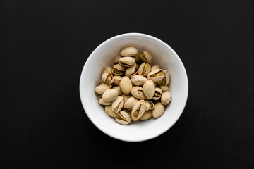 Pistachios in a small plate on a black table. Pistachio is a healthy vegetarian protein nutritious food. Natural nuts snacks.
