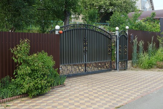 black iron gate and brown metal fence on the sidewalk on the street in green vegetation